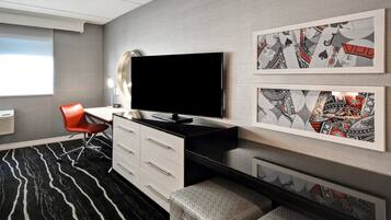 Een moderne hotelkamer met een flatscreen televisie, een rode stoel, een witte kapstok en kunstwerken met een patroon op de muren.