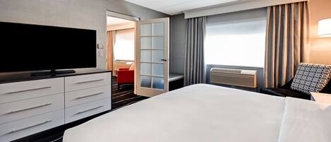 Habitación de hotel con una cama grande, televisor de pantalla plana, cómoda, vestidor y ventana con cortinas.