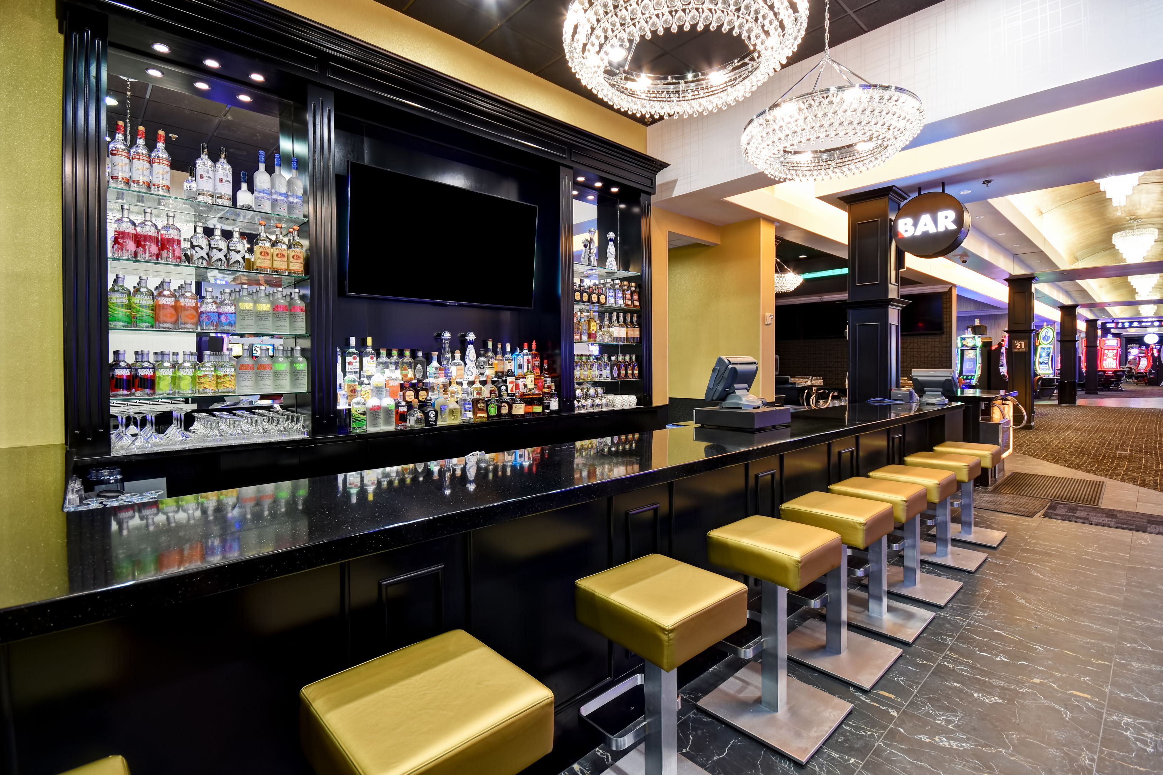 A bar area with a long counter, multiple stools, and a variety of bottles on shelves.