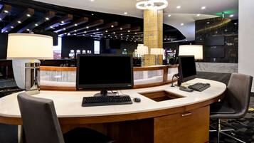 A hotel reception desk with a curved counter, a computer, a telephone, and a seating area with two chairs.