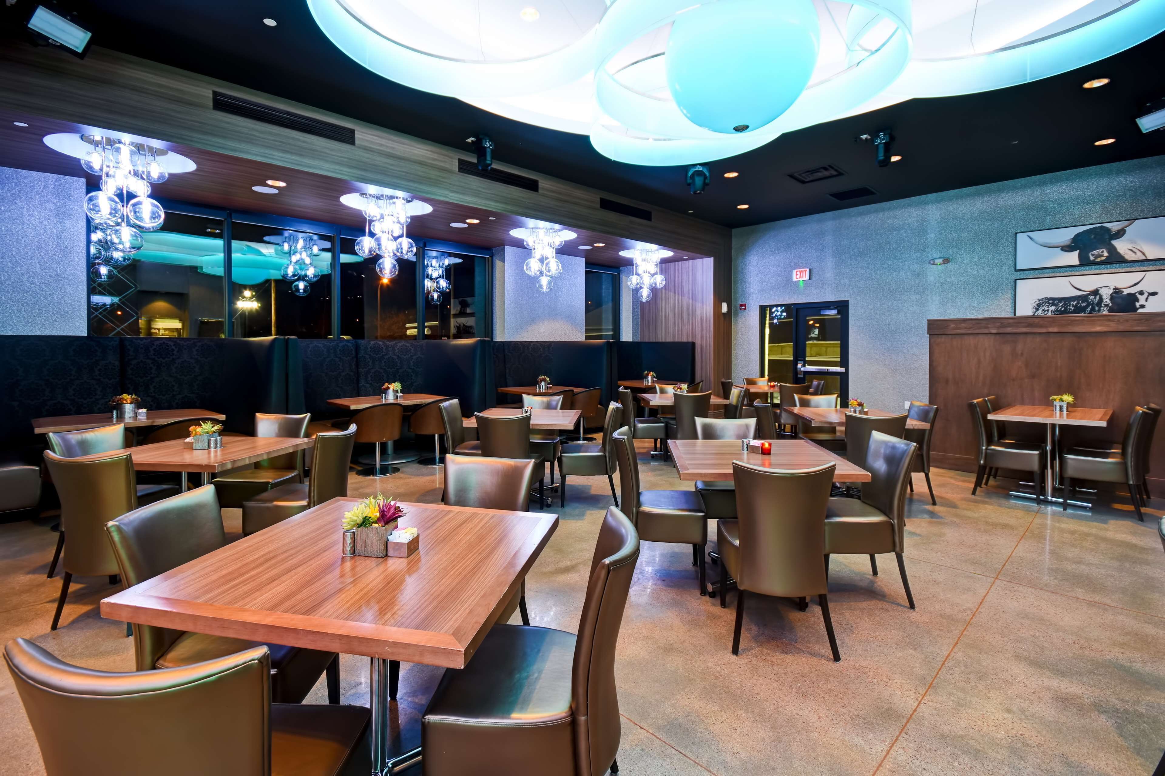 A restaurant with multiple tables and chairs, modern chandeliers, and a large circular light fixture on the ceiling.