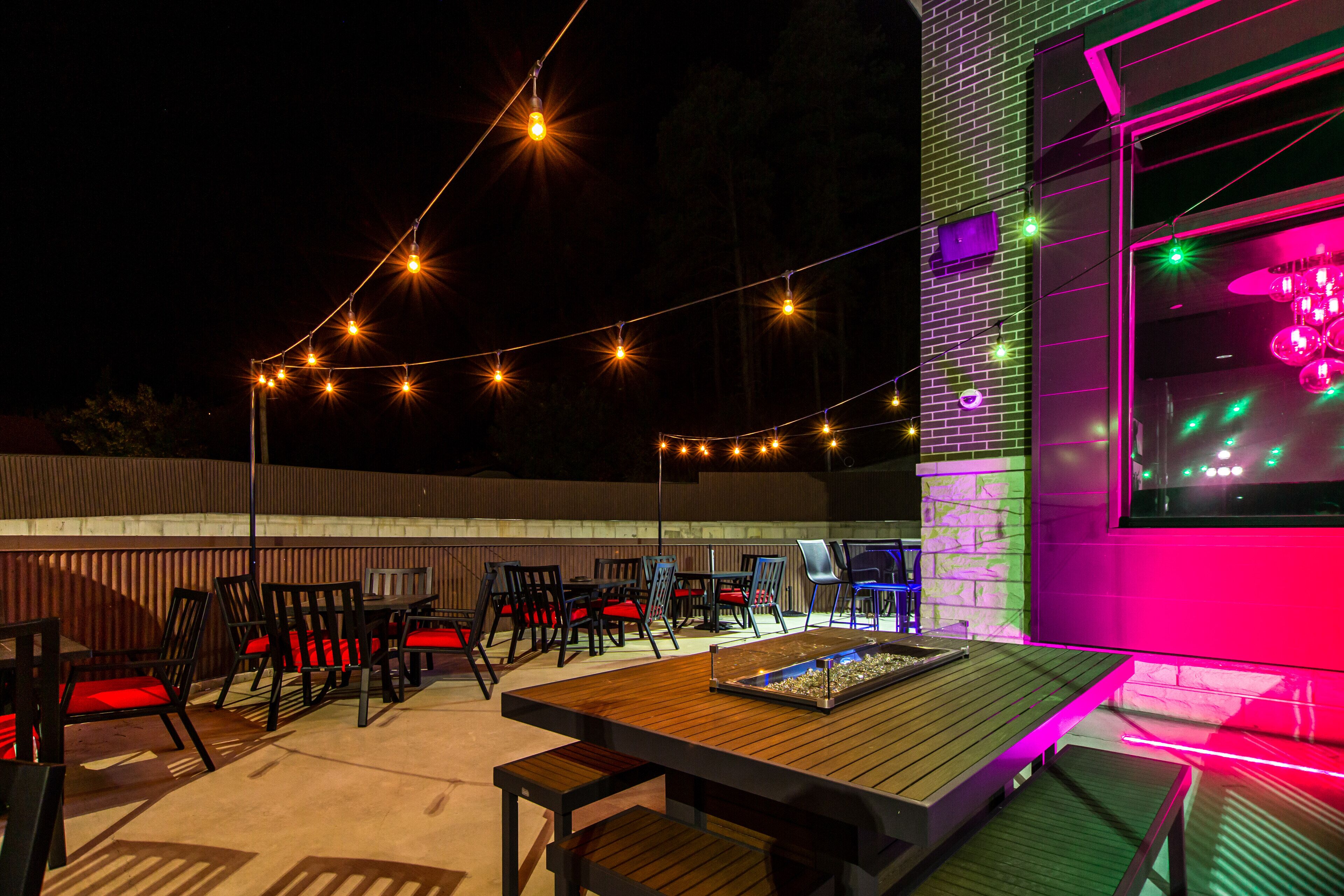 Un patio al aire libre con luces colgantes, mesas y sillas de madera.