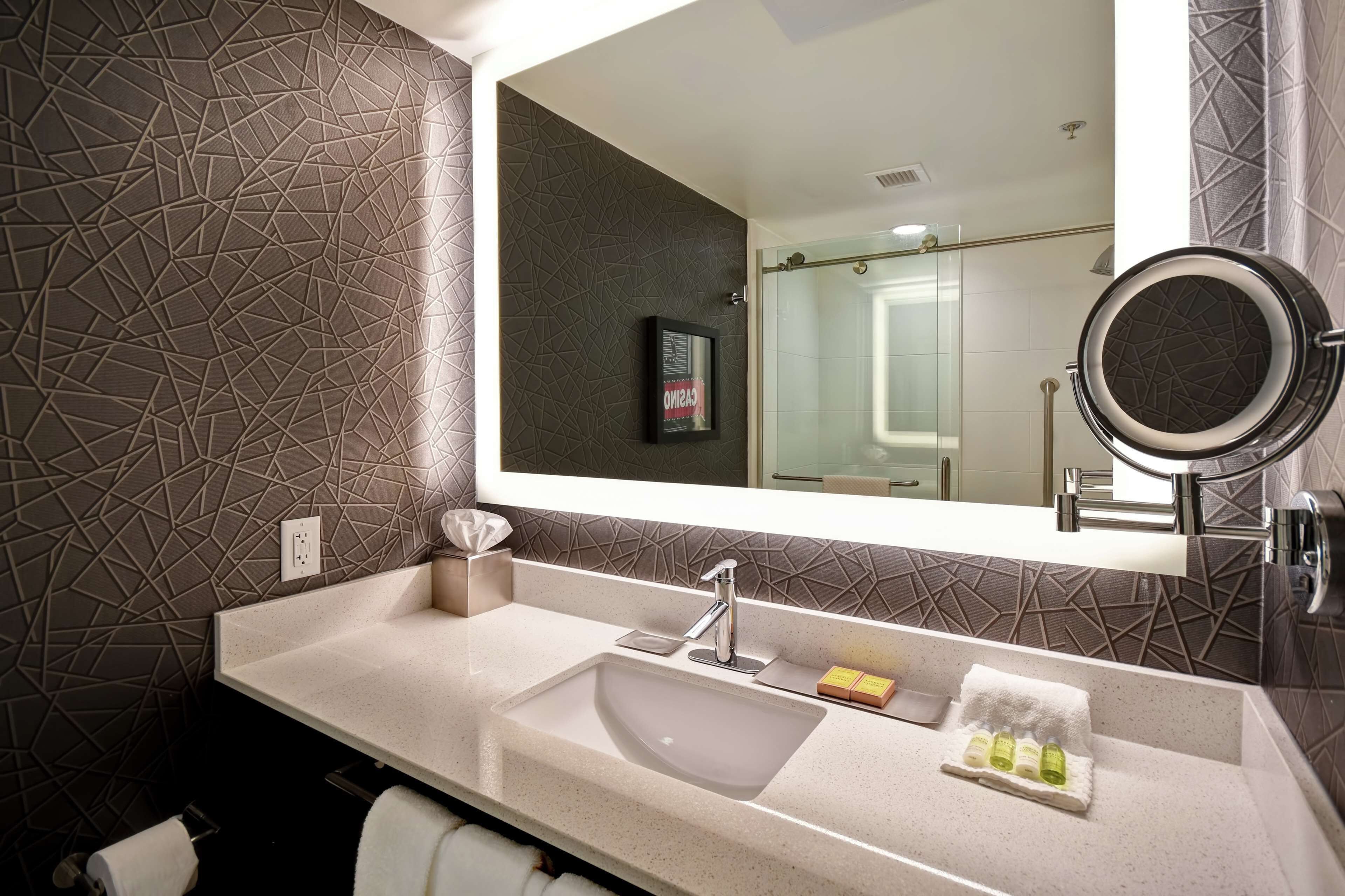 Un baño moderno con un espejo grande, un lavamanos y una cabina de ducha de vidrio.