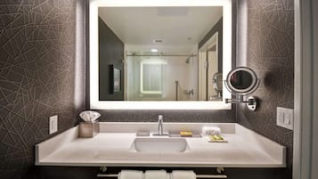 Een moderne badkamer met een grote spiegel, een wastafel en een douche die in de weerspiegeling zichtbaar is.