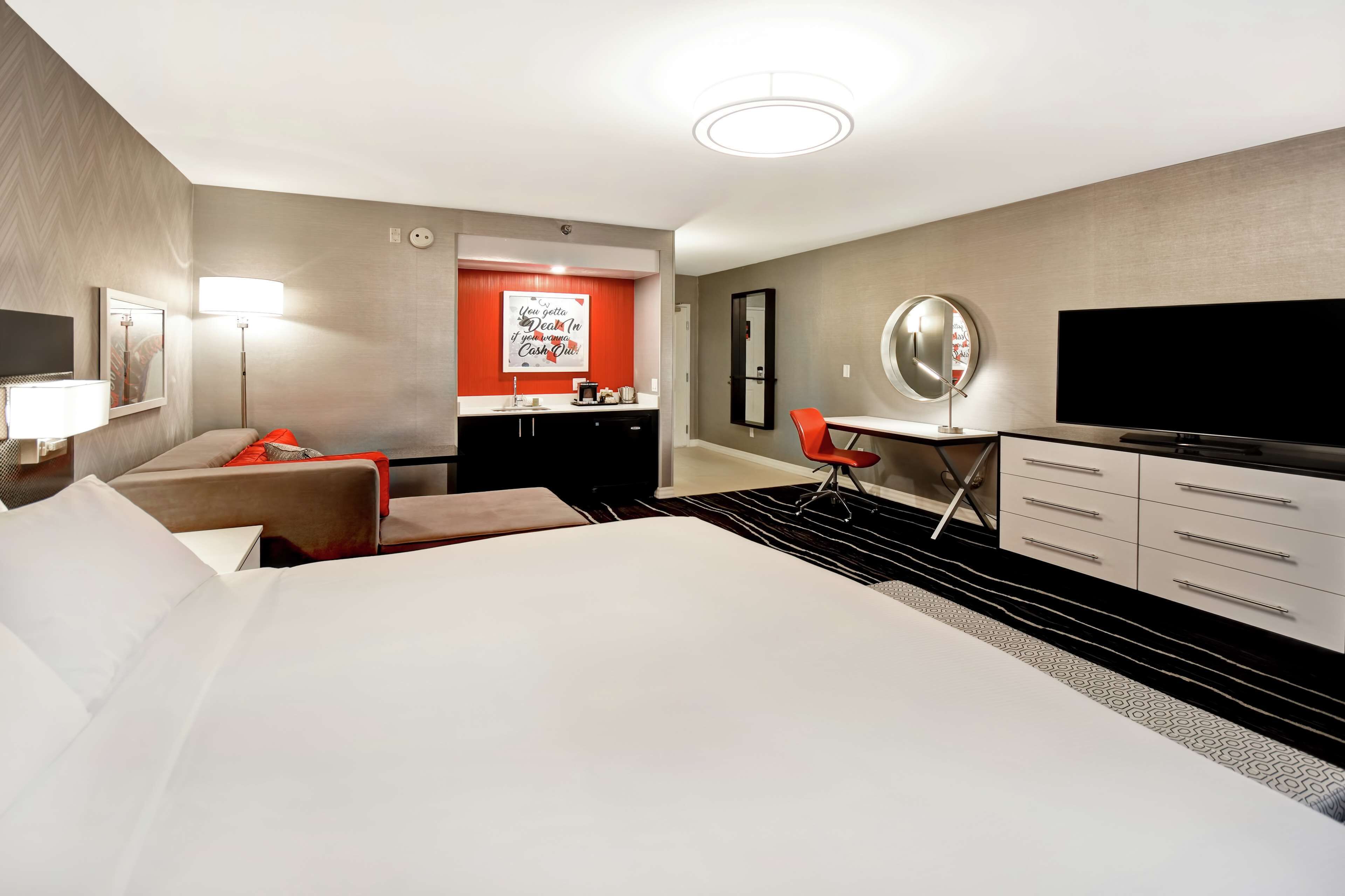 A hotel room with a large bed, a desk, a chair, a TV, and a minibar.