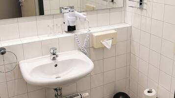 Un baño con lavamanos blanco, un espejo, un secador de pelo y un dispensador de toallas.