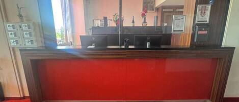 Una recepción con un mostrador rojo, un teléfono y una computadora.