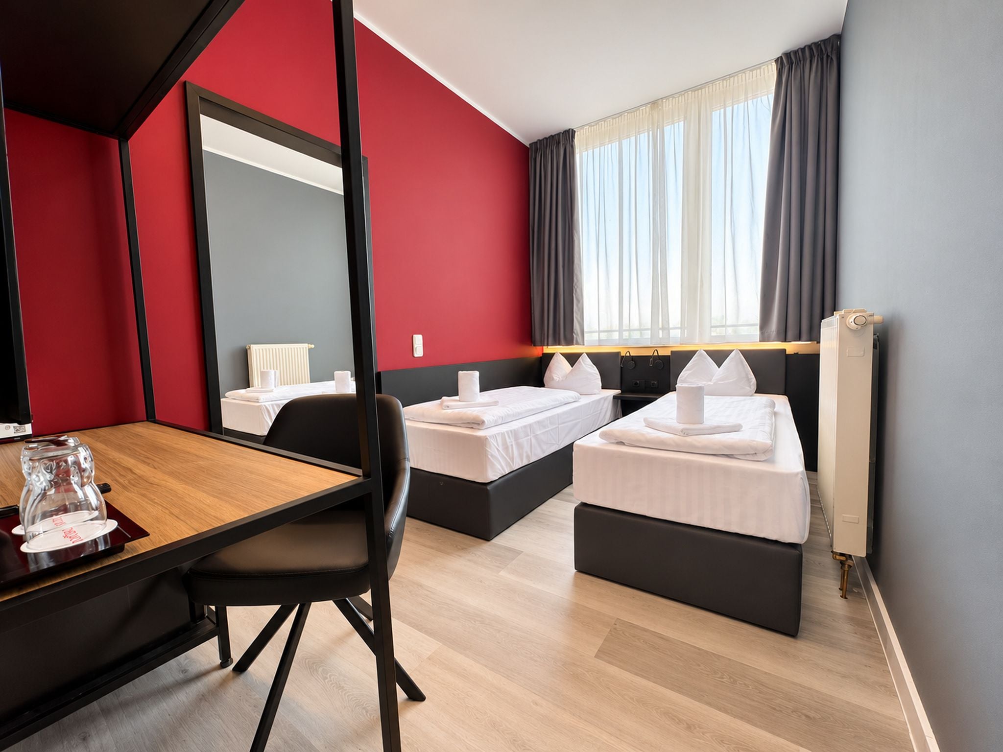 A hotel room with two beds, a wooden desk, and a large mirror.