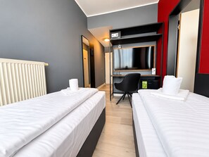A hotel room with two beds, a desk, a chair, a TV, and a radiator. - DORMERO Express Hotel Passau (Passau)