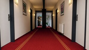 Un pasillo de hotel con alfombra roja, obras de arte enmarcadas en las paredes y un radiador a la derecha.