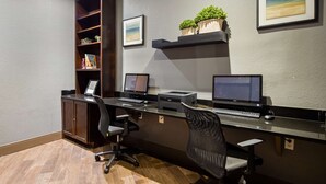 A modern office space with a long desk, two monitors, a printer, and a bookshelf with plants. - Best Western Plus Hill Country Suites (San Antonio)
