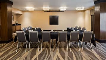 Una sala de conferencias con una larga mesa, sillas y una pantalla para proyector.