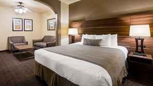 A hotel room with a large bed, two armchairs, a small table, and a ceiling fan. - Best Western Plus Hill Country Suites (San Antonio)