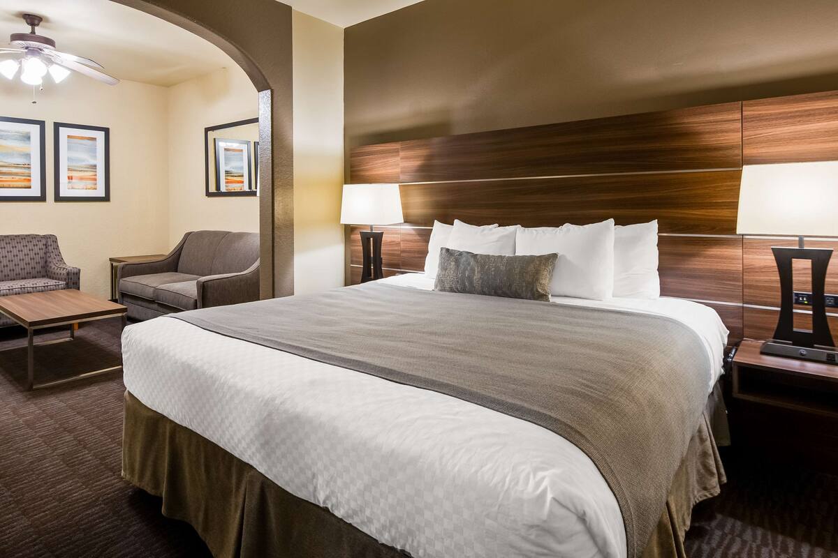 Een hotelkamer met een groot bed, twee fauteuils, een tafeltje en een plafondventilator.