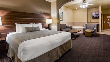 Quarto de hotel com uma cama grande, uma escrivaninha, uma cadeira, uma mesinha, um sofá, um micro-ondas e um ventilador de teto.