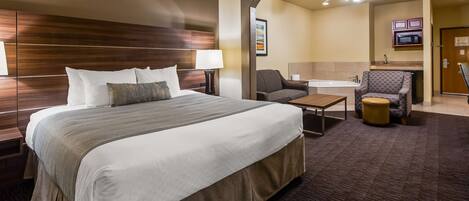 Ein Hotelzimmer mit einem großen Bett, einem Schreibtisch, einem Sessel, einem kleinen Tisch, einer Couch, einer Mikrowelle und einem Deckenventilator.