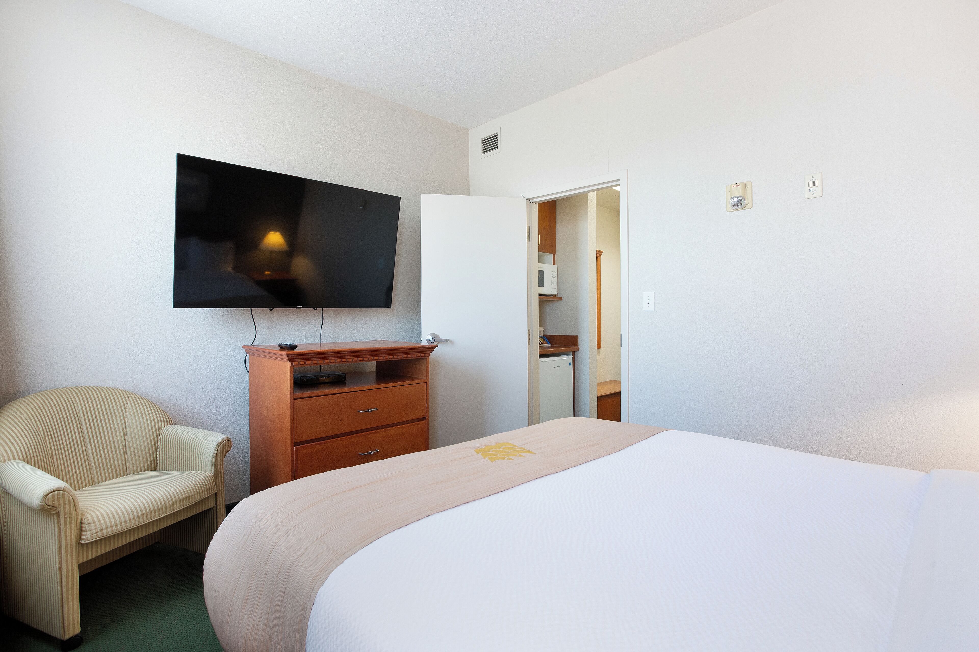 Une chambre d’hôtel avec un lit, un téléviseur fixé au mur, une commode en bois et une chaise.