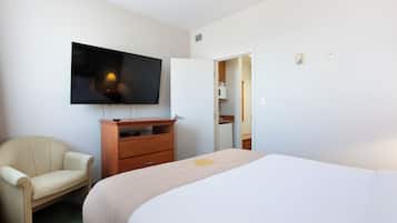 Une chambre d’hôtel avec un lit, un téléviseur fixé au mur, une commode en bois et une chaise.