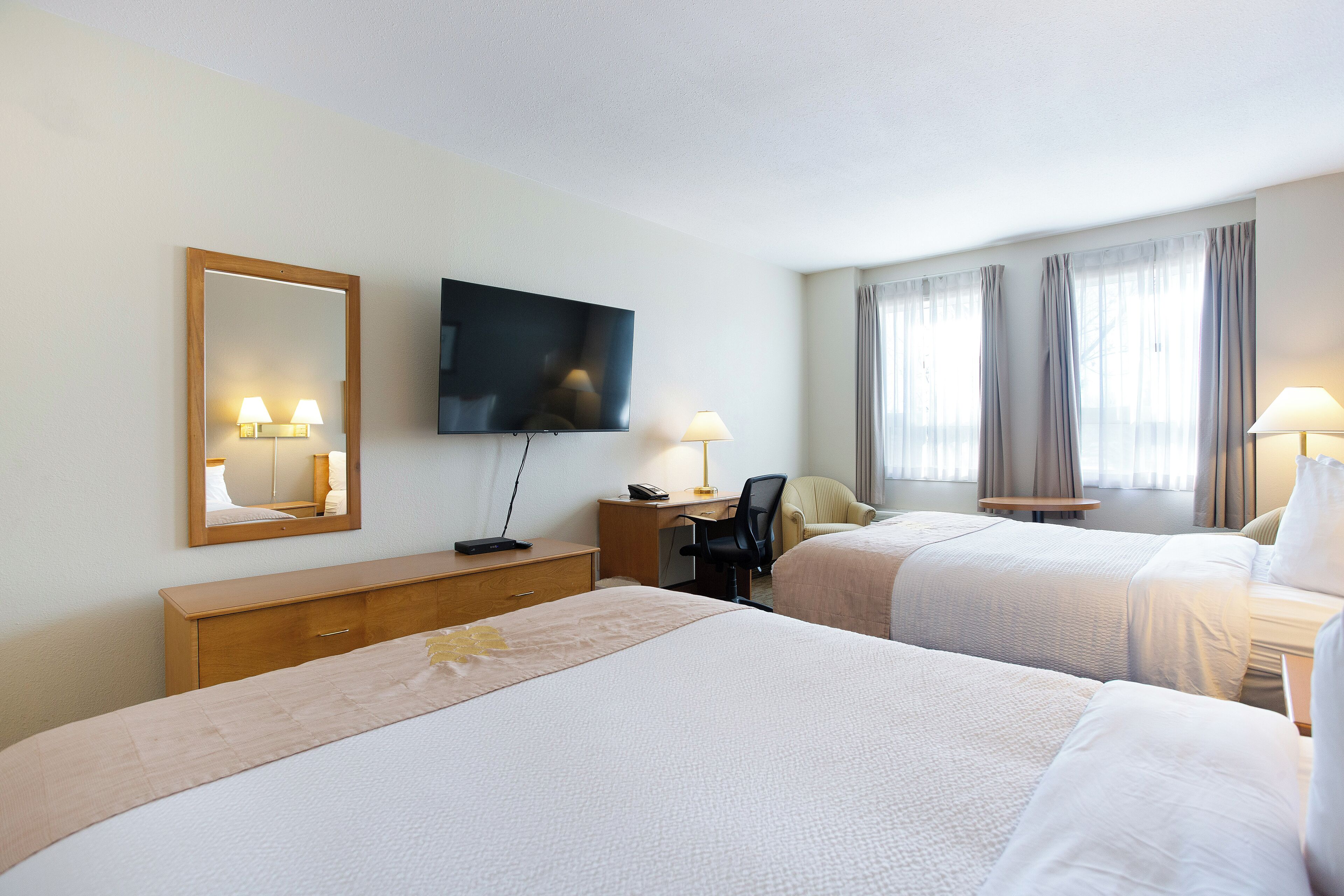 Ett hotellrum med två sängar, ett skrivbord, en stol, en tv och ett fönster med gardiner.