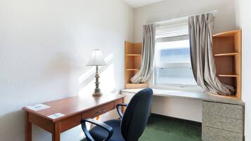 Habitació petita i ben ordenada amb escriptori, cadira, làmpada, finestra amb cortines i prestatge incorporat.