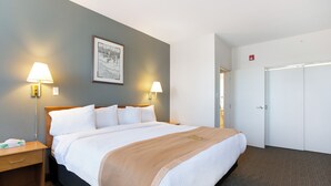 Habitación de hotel con una cama grande, dos lámparas de noche, un cuadro enmarcado en la pared y una puerta cerrada.