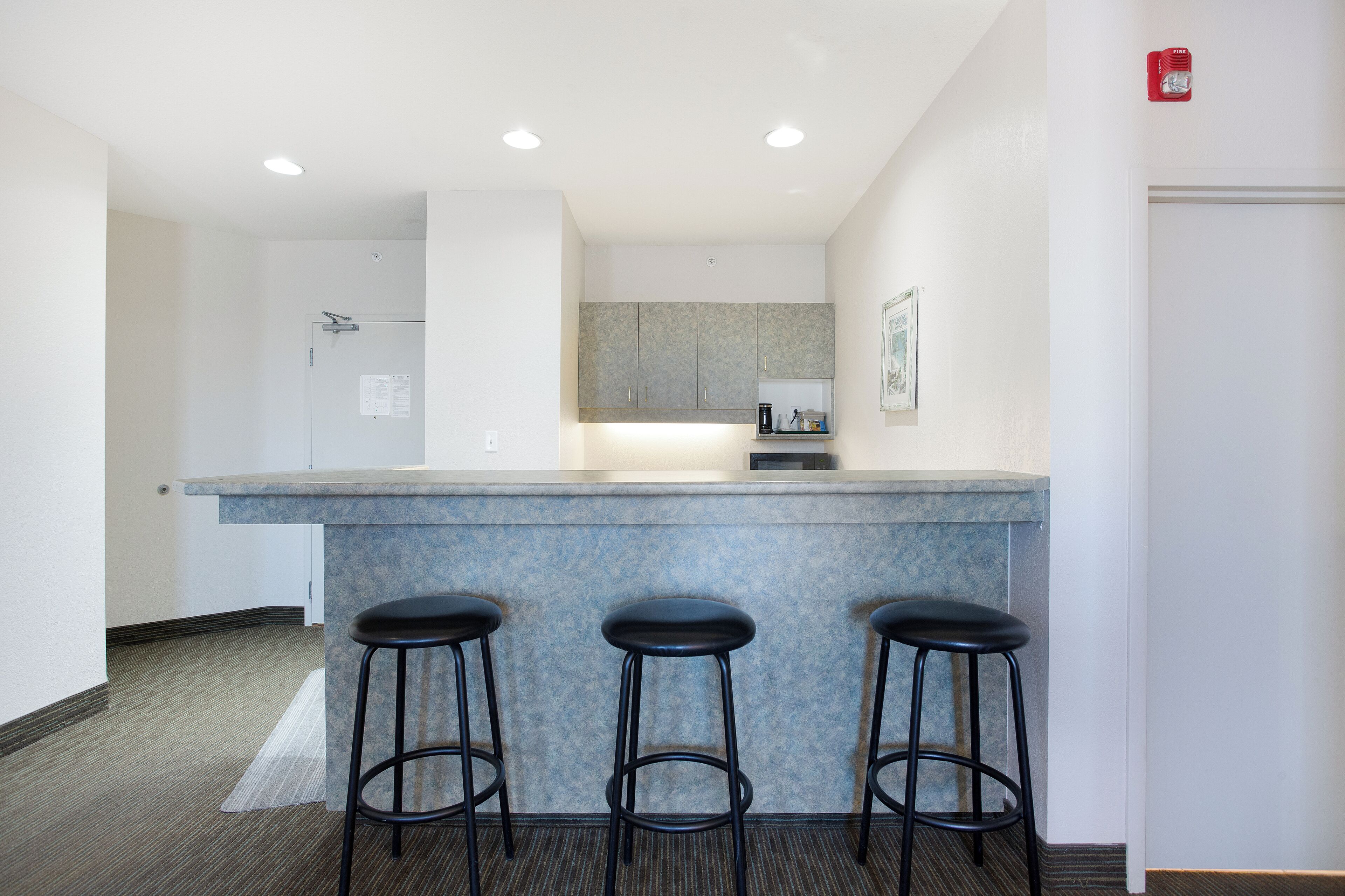 A modern kitchen with a marble countertop, three black bar stools, and a small coffee station.