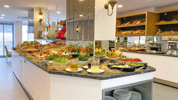 A buffet area with various food items, decorative plants, and a modern kitchen in the background. - Best Western Plus Khan Hotel (Antalya)