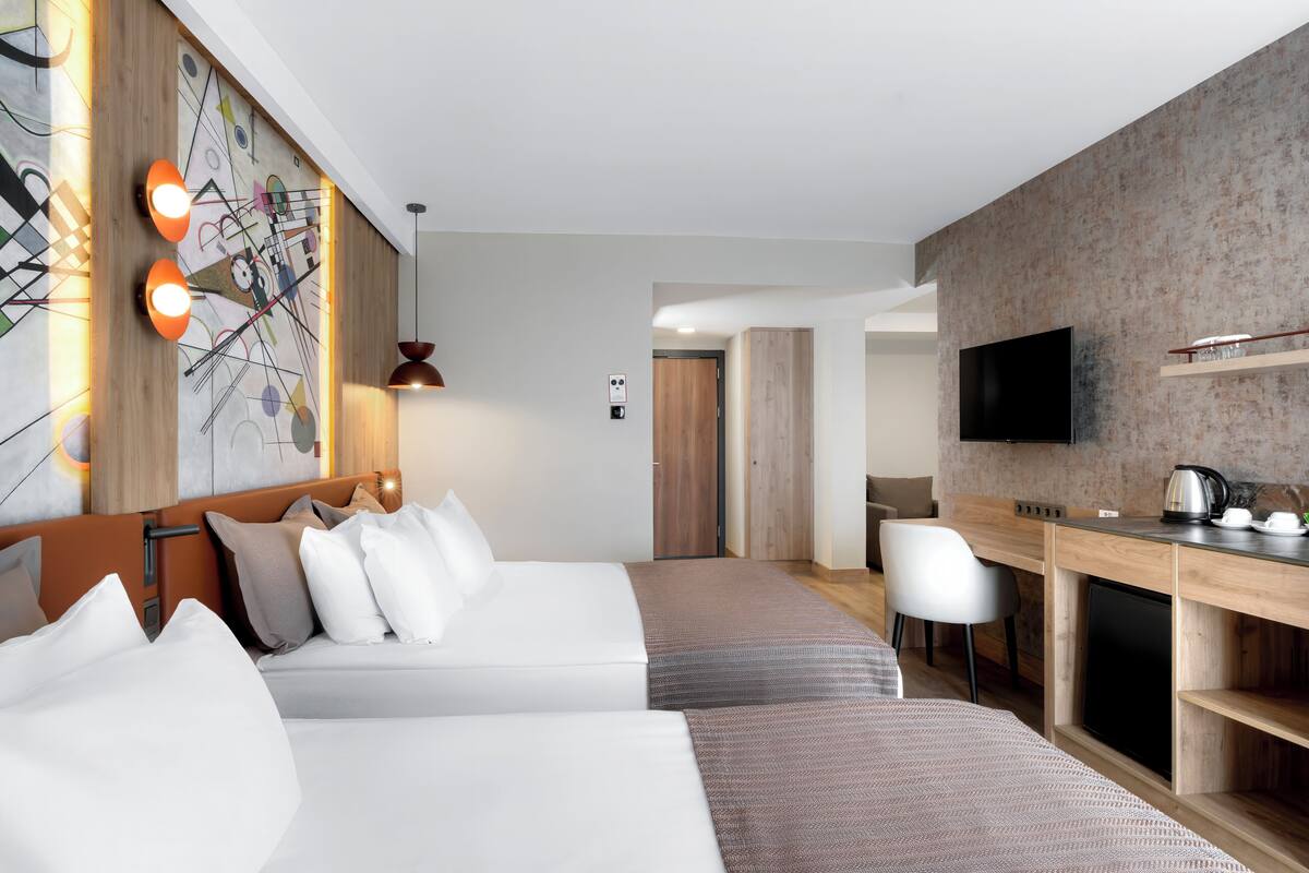 A hotel room with a bed, a desk, a chair, a TV, and a kitchen area.