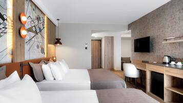 A hotel room with a bed, a desk, a chair, a TV, and a kitchen area.