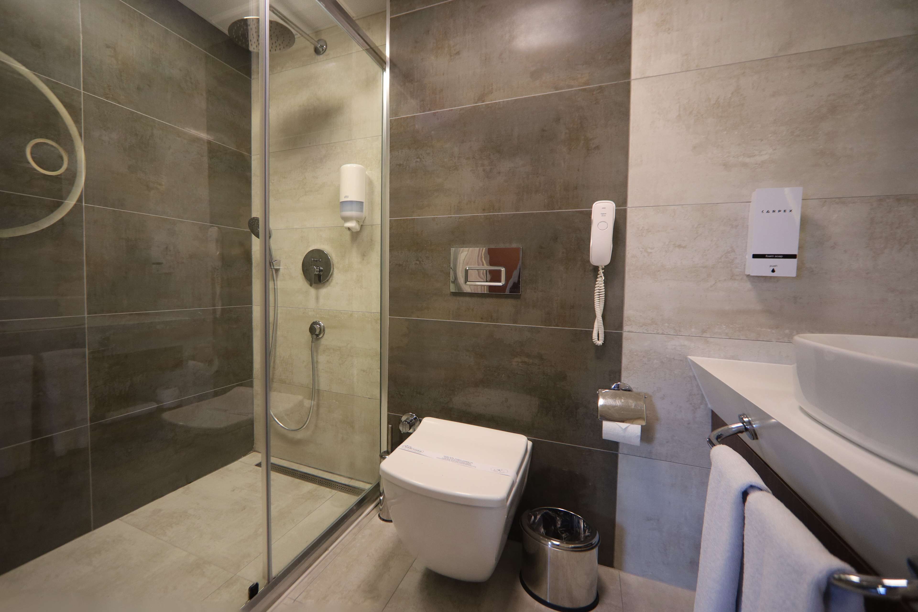 A modern bathroom with a glass shower enclosure, a toilet, a sink, and a telephone.