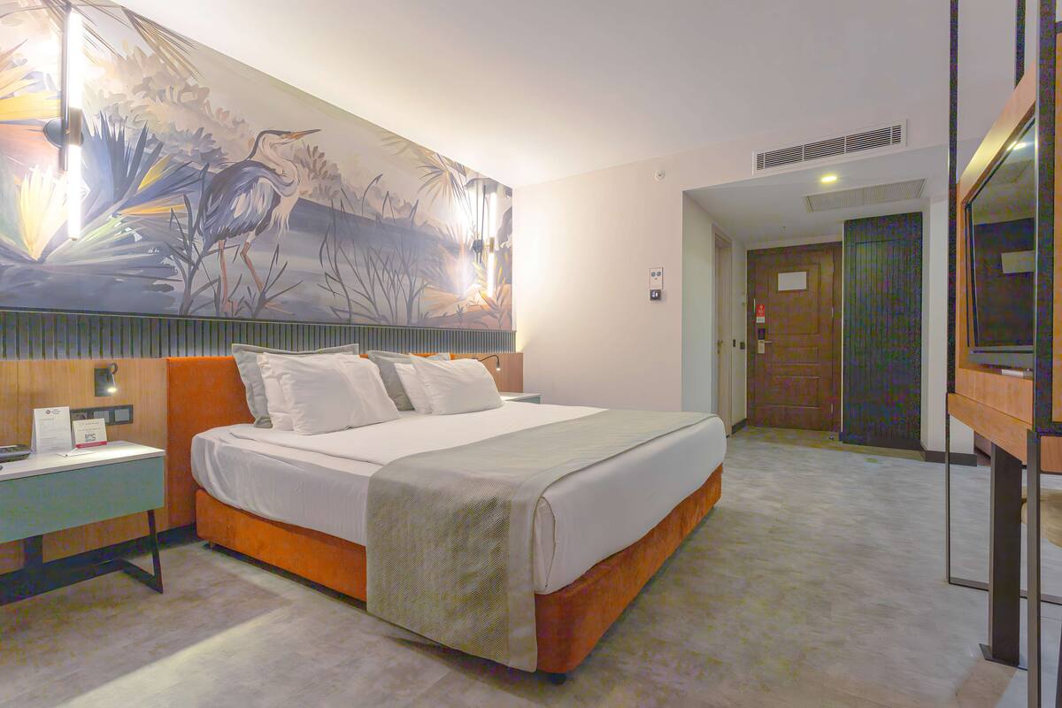 Hotelkamer met een groot bed, nachtkastje, muurschildering en een deur naar de badkamer.