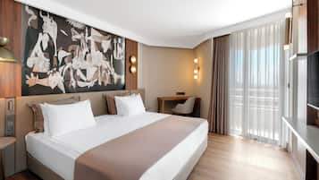 A hotel room with a large bed, a desk, a chair, a TV, and a large window with curtains.