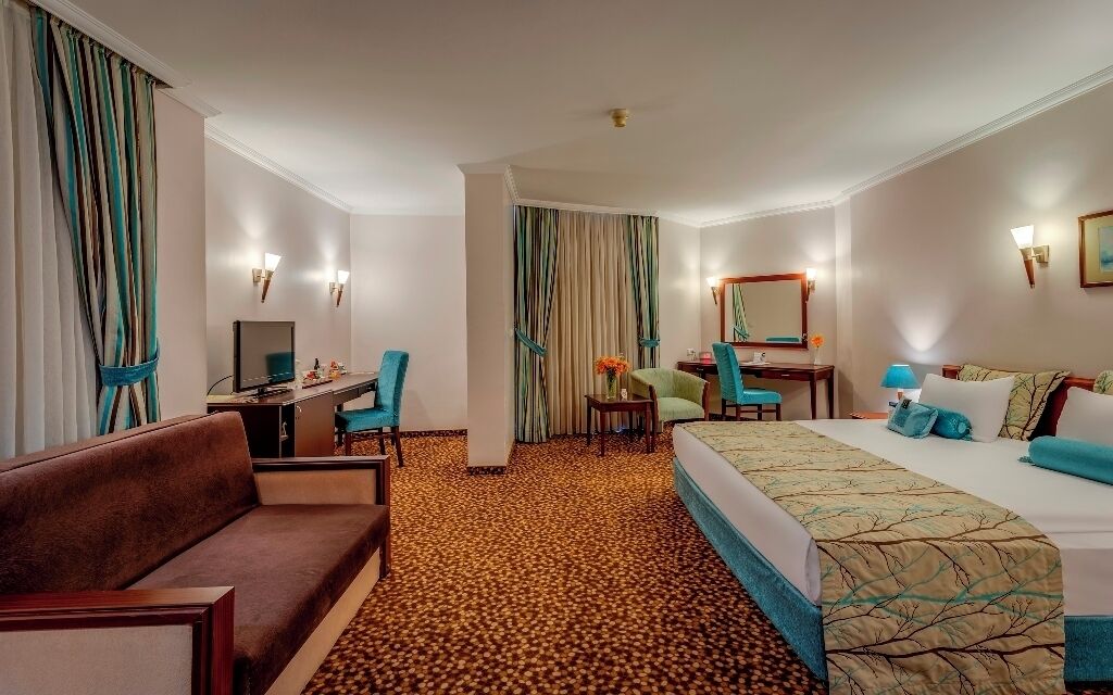 A hotel room with a sofa, a bed, a desk, a chair, a small table, and a mirror.