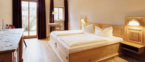 A hotel room with a wooden bed, a desk, a chair, a small table, and a window with curtains.