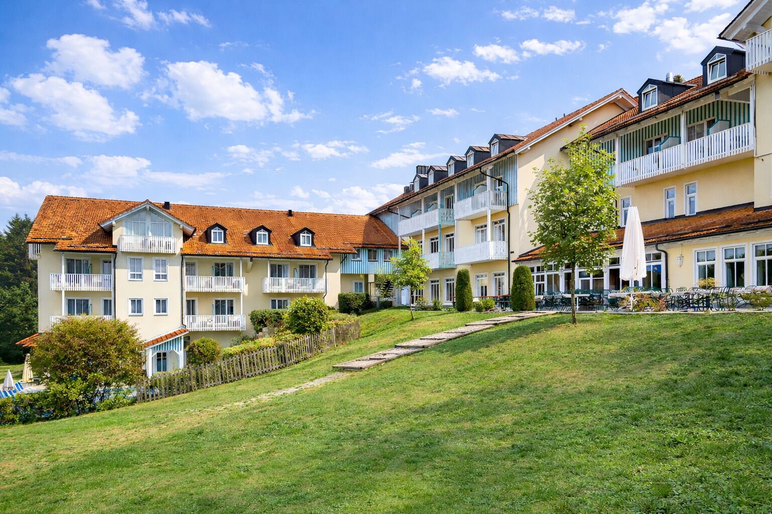 Un hôtel à plusieurs étages, doté de balcons, d’une pelouse verdoyante et surplombant un ciel dégagé.