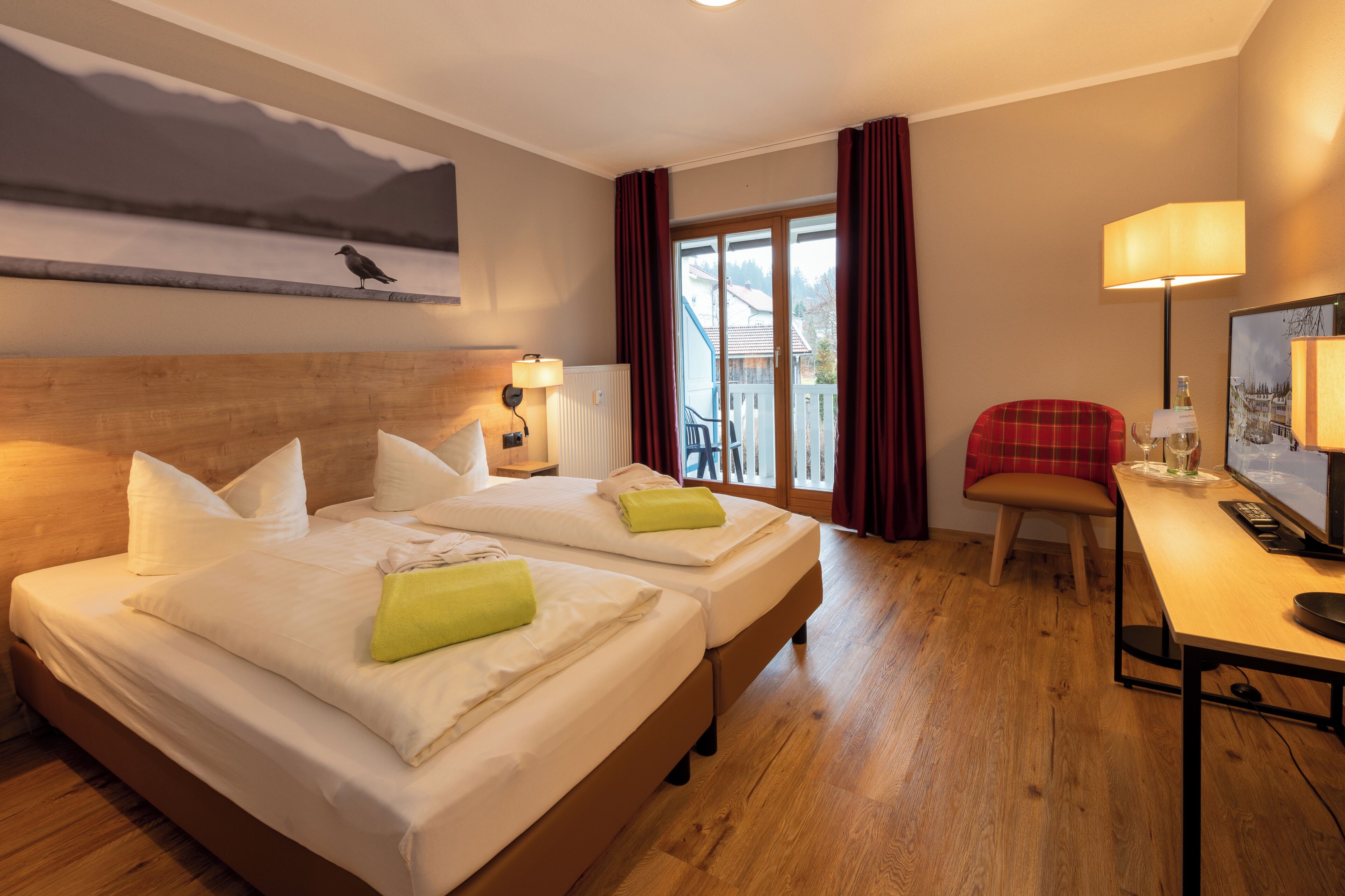 Habitación de hotel con dos camas, un escritorio con computadora, una silla, una lámpara y vista al exterior.