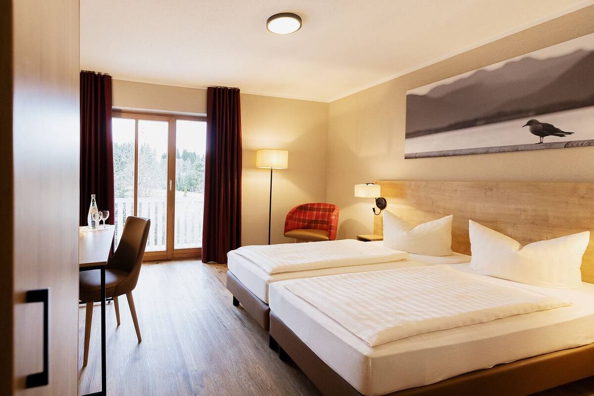 A hotel room with two beds, a desk, and a chair.