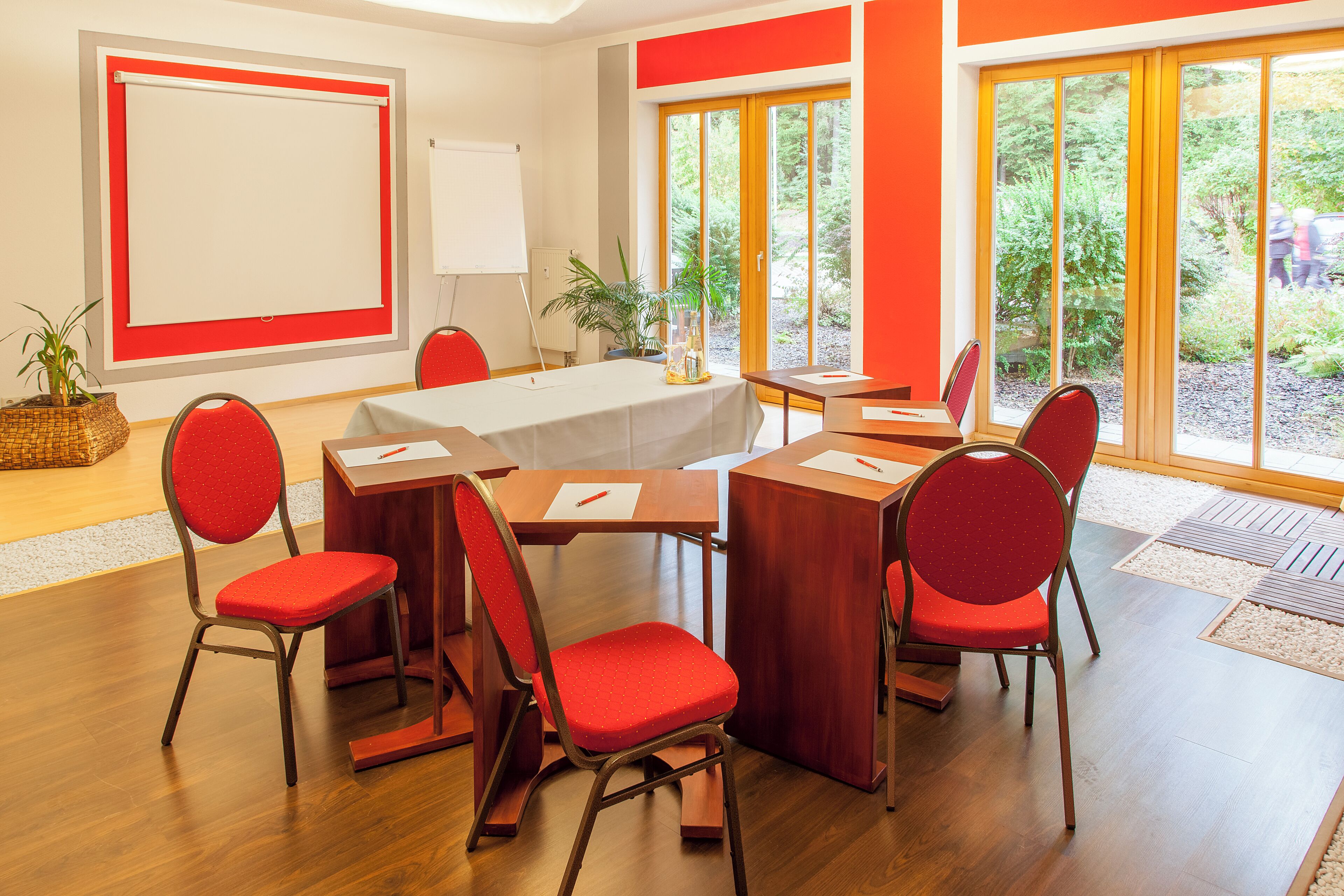 A conference room with a whiteboard, a table with papers, and red chairs.