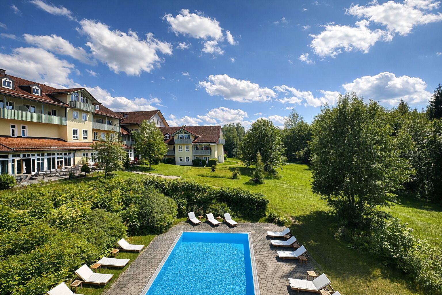 A hotel with a swimming pool, lounge chairs, and a well-maintained garden.