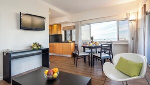 A modern hotel room with a dining area, a kitchen, and a large window offering a city view. - Alvor Atlântico Residences (Portimão)