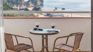 A balcony with two wicker chairs and a small table, overlooking a beach with rocky cliffs and the ocean. - Alvor Atlântico Residences (Portimão)