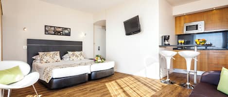Una habitación de hotel moderna con cama, zona de estar, kitchenette y televisor de pantalla plana.
