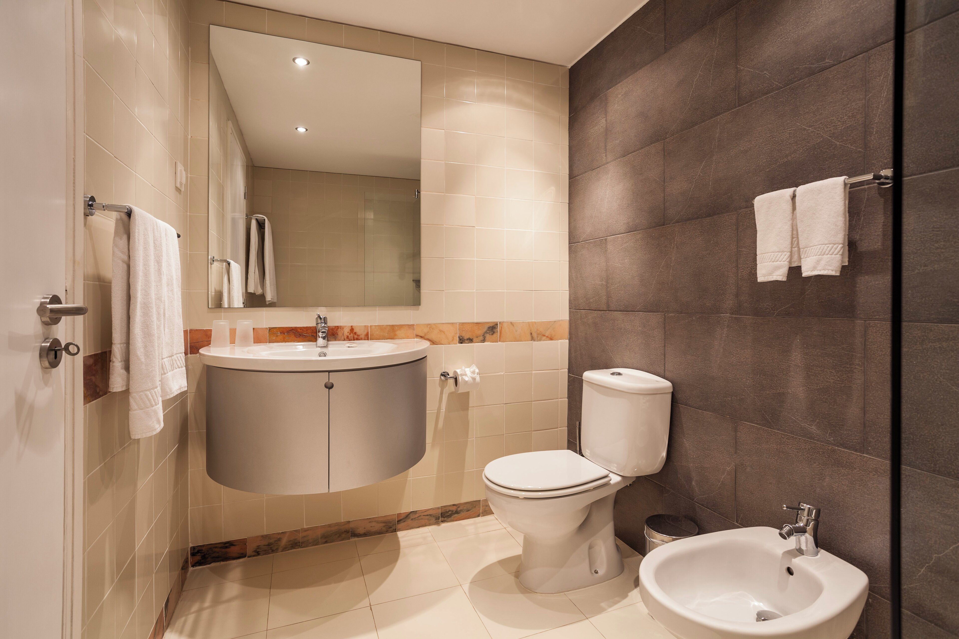 A modern bathroom with a toilet, bidet, sink, and mirror.