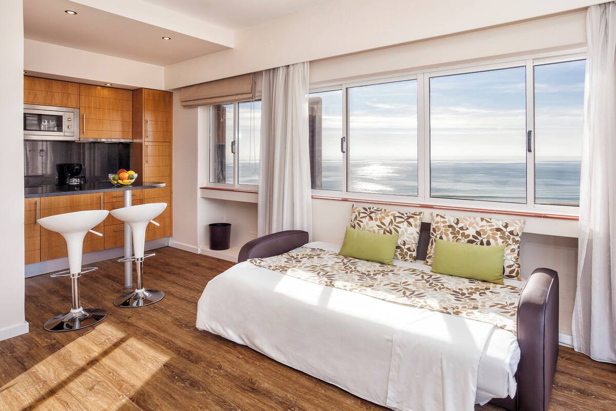 Une chambre d’hôtel moderne dotée d’un grand lit, d’une kitchenette et offrant une vue sur la mer.