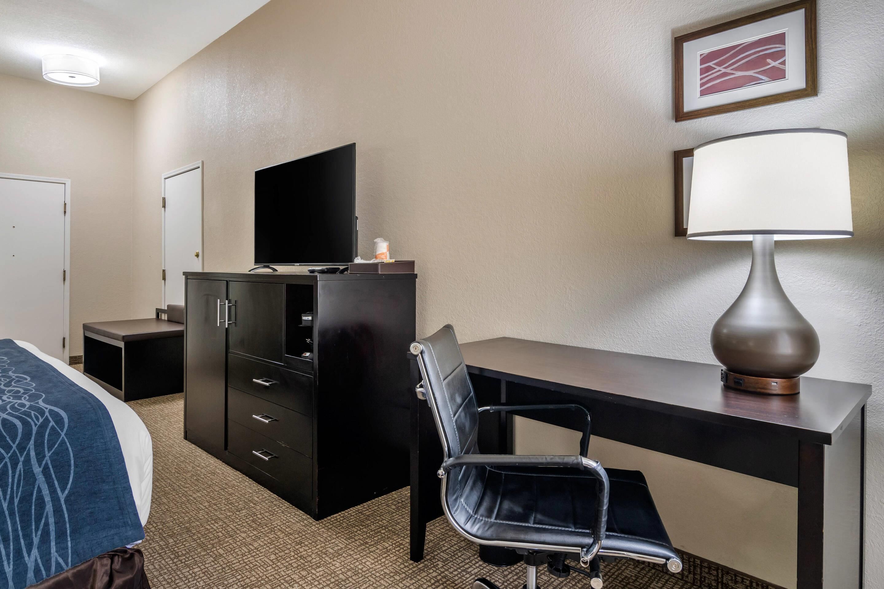 Une chambre d’hôtel comprenant un lit, un bureau avec une chaise, une télévision, une lampe et une armoire.