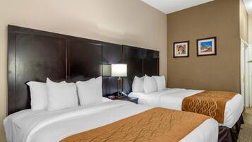 A hotel room with two beds, a large dark headboard, a nightstand with a lamp, and two framed pictures on the wall.