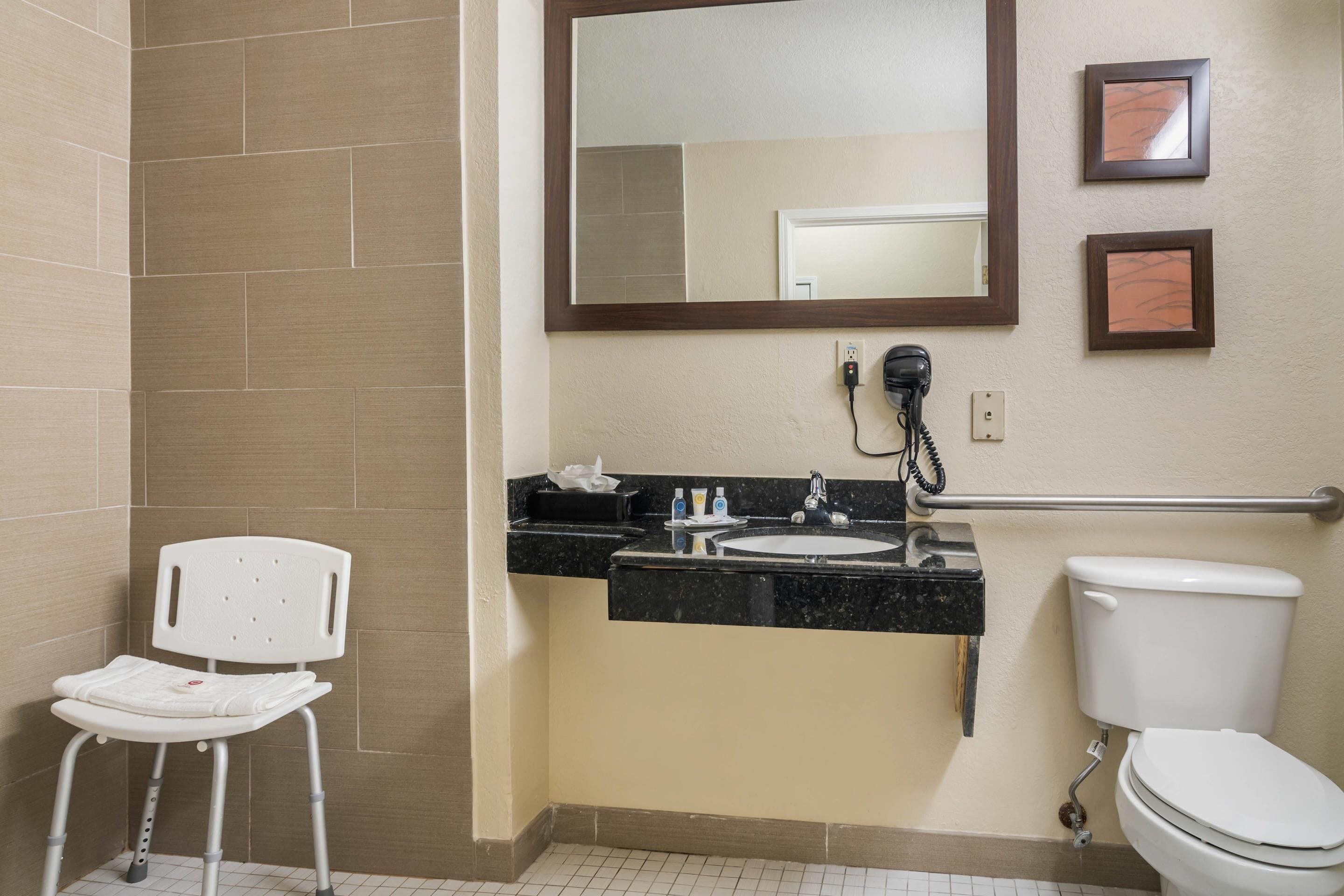 Un bagno con il water bianco, un lavabo con piano nero, uno specchio sopra il lavabo e una sedia bianca.