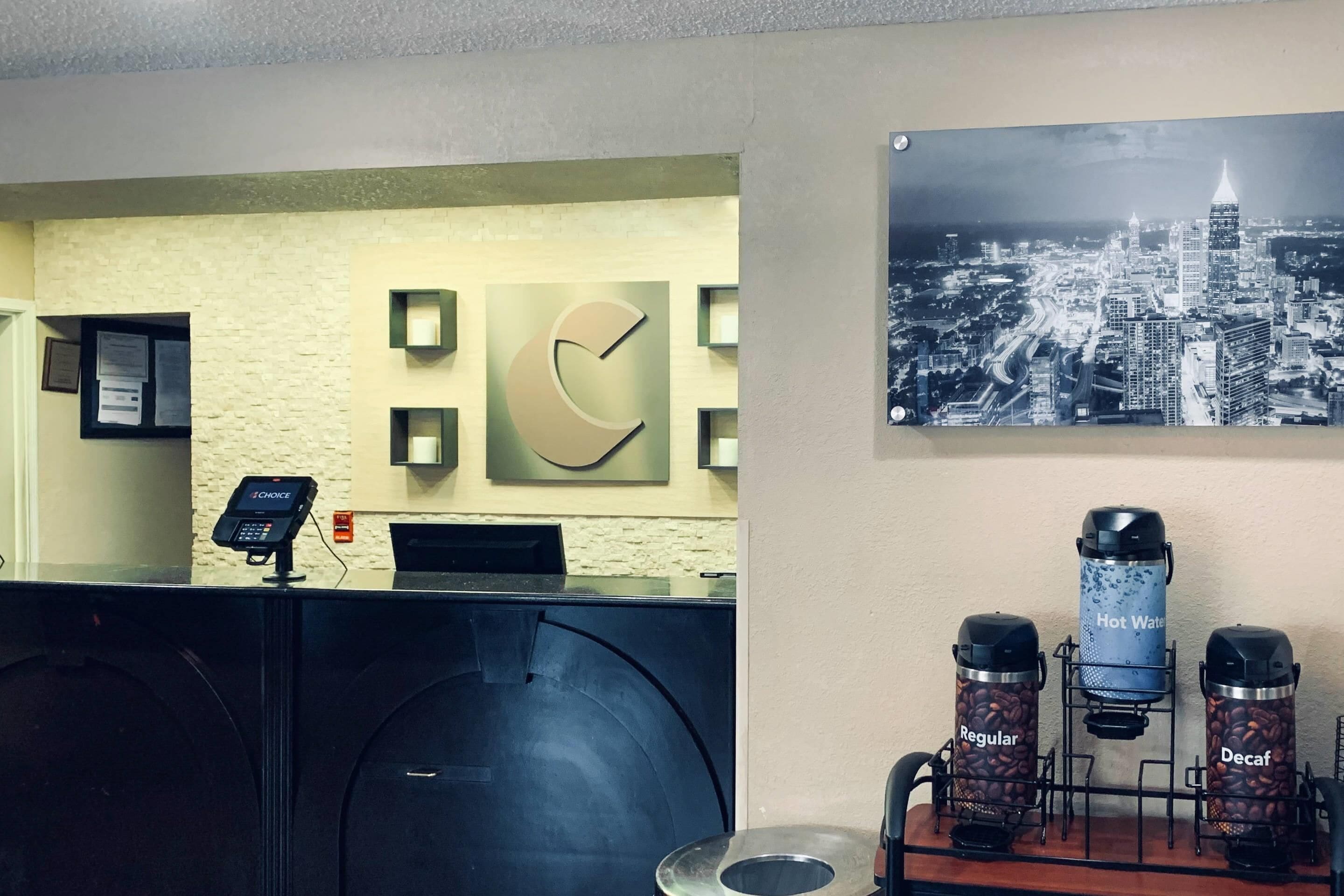 Een hotel receptie met een digitaal betaalterminal, een klok en een koffiehoek met opties voor koffieloze en gewone koffie.