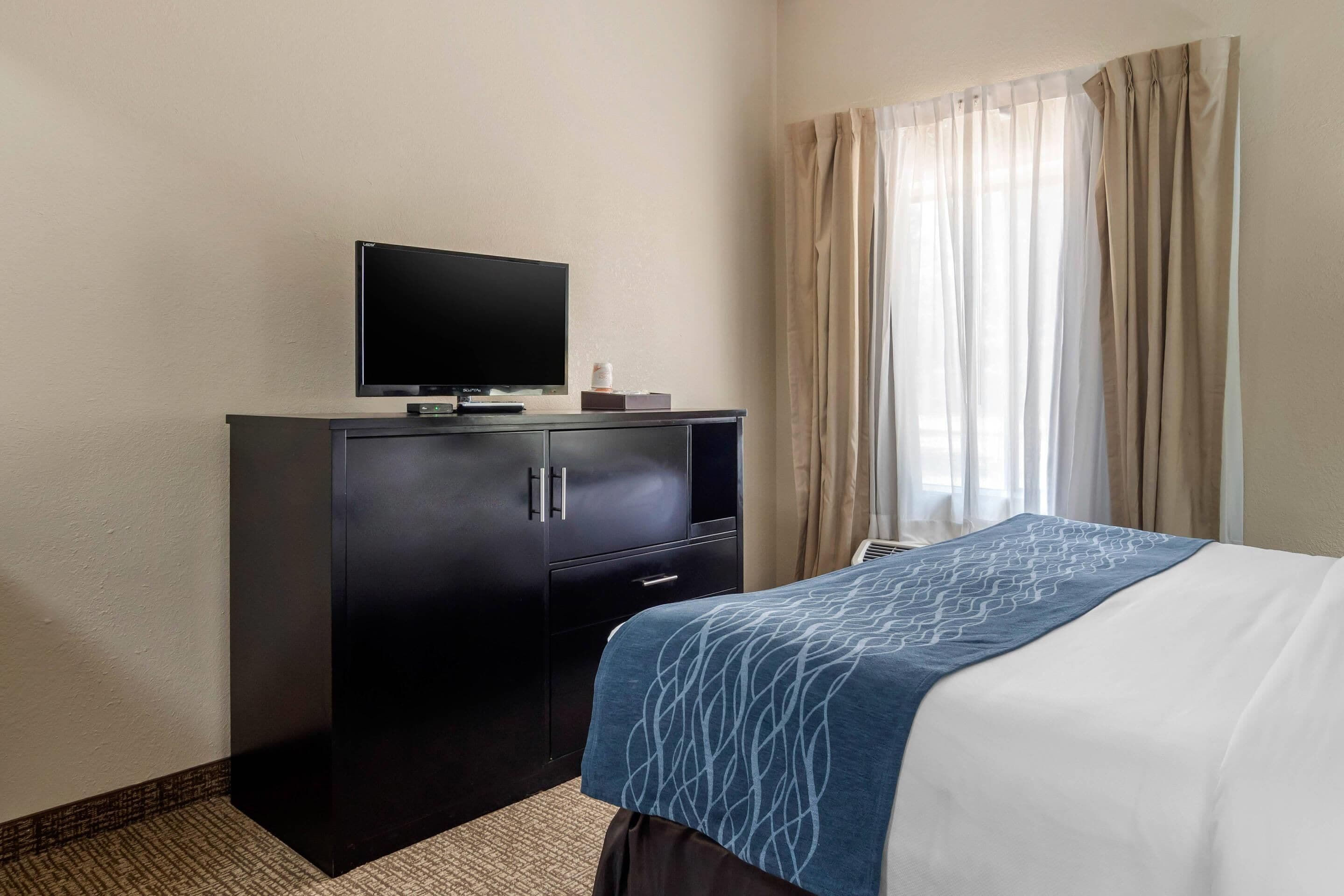 A hotel room with a bed, a TV on a cabinet, and a window with curtains.