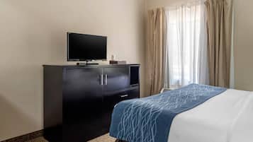 A hotel room with a bed, a TV on a cabinet, and a window with curtains.